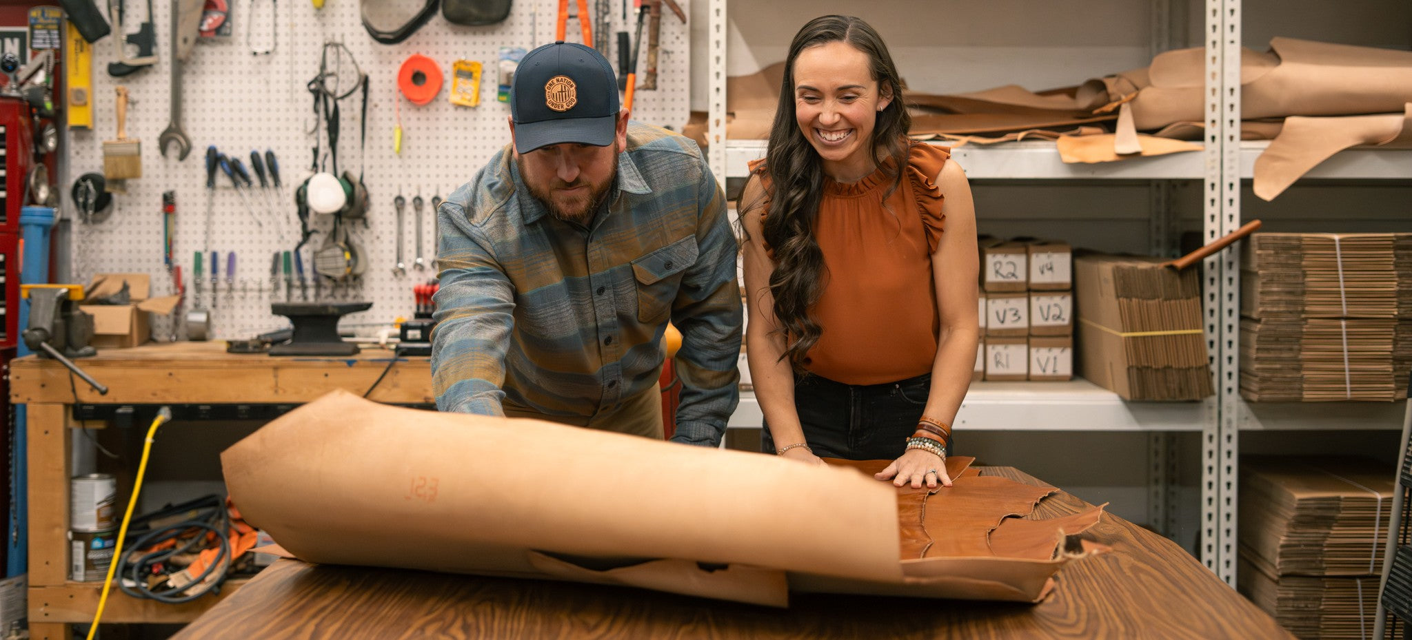 Two people in a workshop setting, with one person rolling out leather
