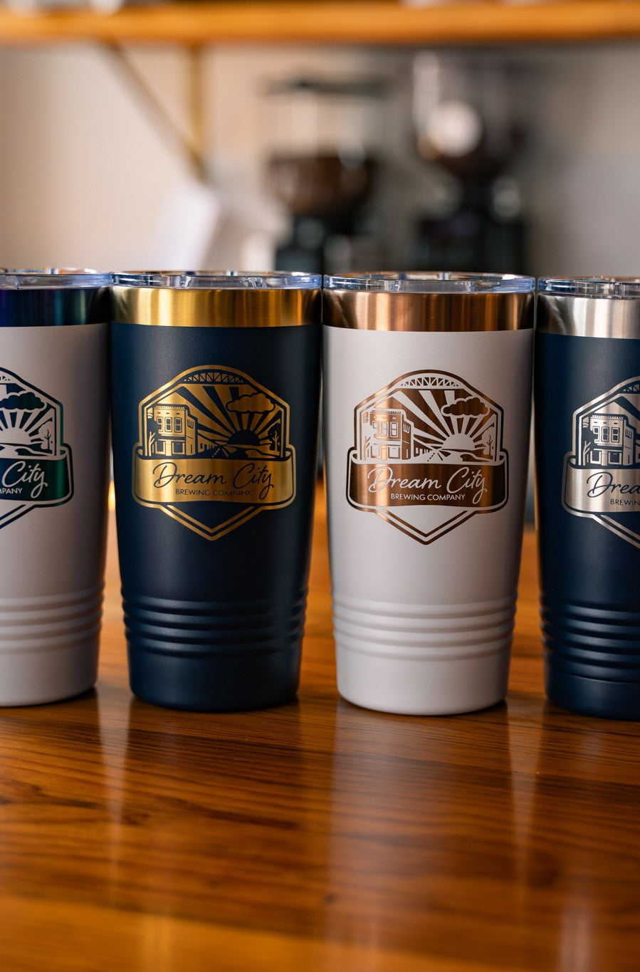 Four 20oz tumblers with branded designs on a wooden surface