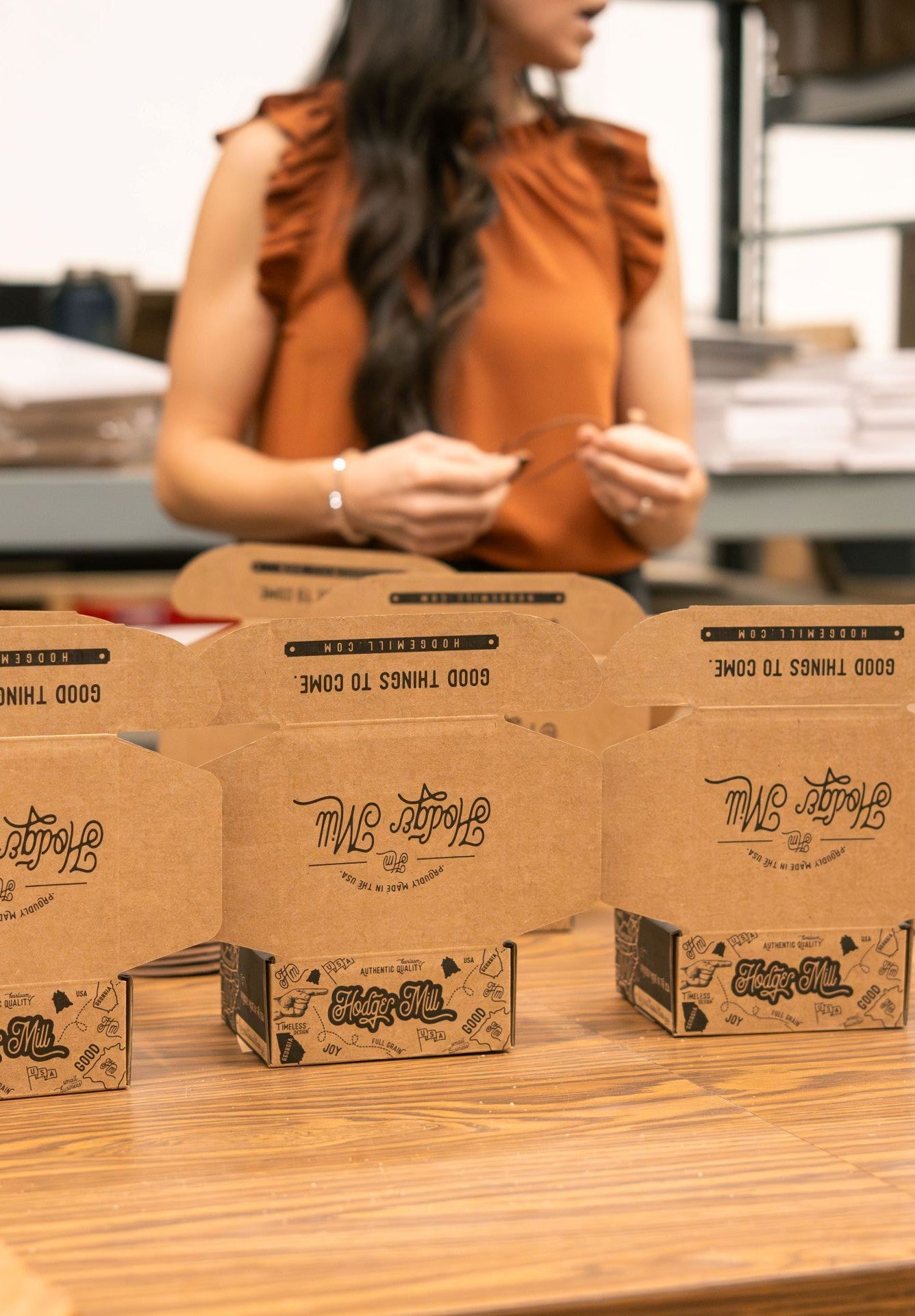 Person standing behind a row of branded cardboard boxes on a table.